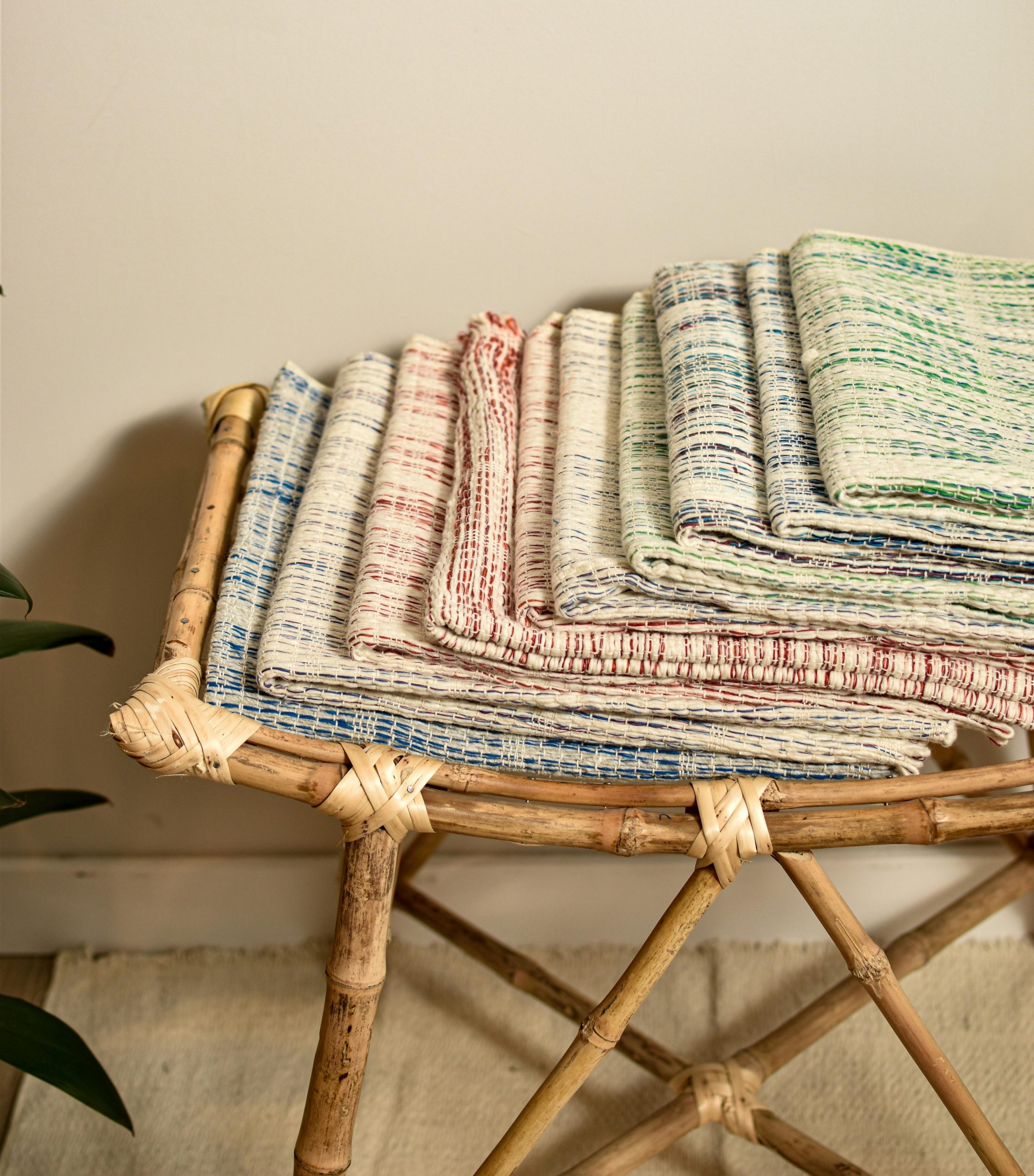 A stack of colorful handwoven textiles on a bamboo chair, showcasing traditional craftsmanship.